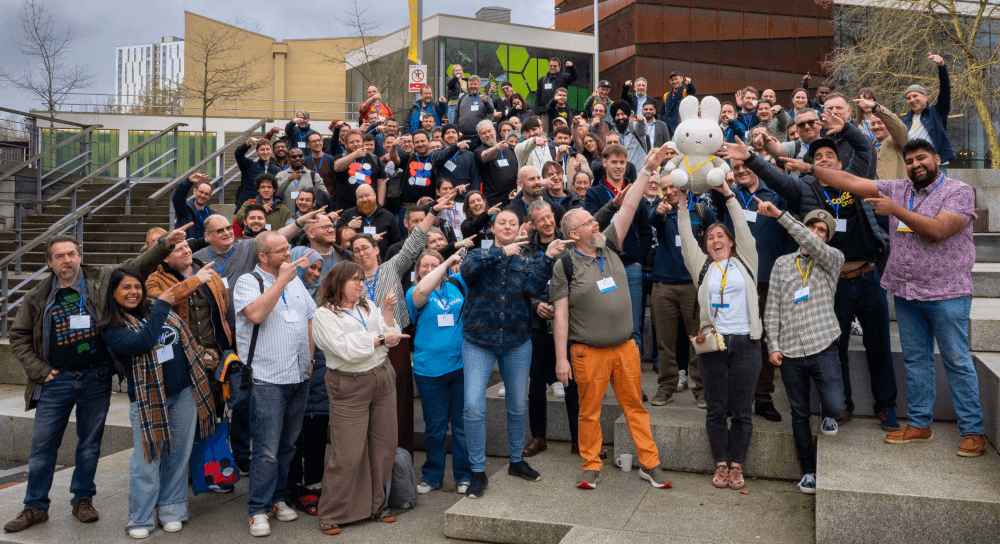 The group photo for DrupalCamp England 2026. In this image everyone is pointing at Miffy, the mascot for DrupalCon Europe 2026.
