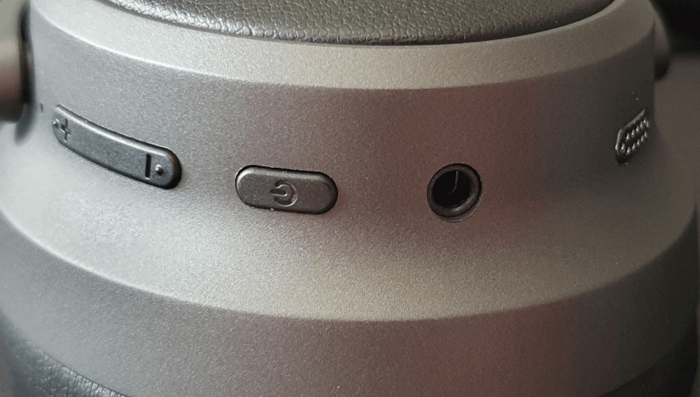 A close up of the right hand side buttons and connection of the Kiwi Ears Ardor. Showing the volume controls, the power button, the AUX input and one of the microphones for active noise cancelling.