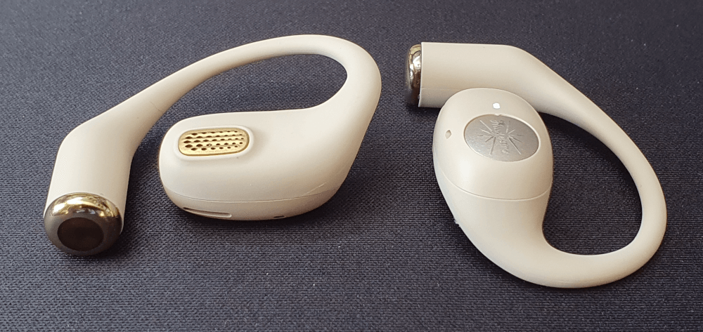 The Kiwi Ears Spark earphones, sat on their own on a black fabric surface. One earphone is facing up, showing the speaker hole on the underside of the earphone.