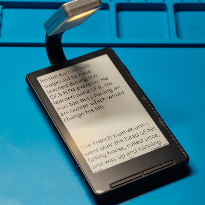The X4 ereader, with a light attached to the back. The light is on a stick that goes over the top of the device and points to the screen. The screen contains some text from a book.